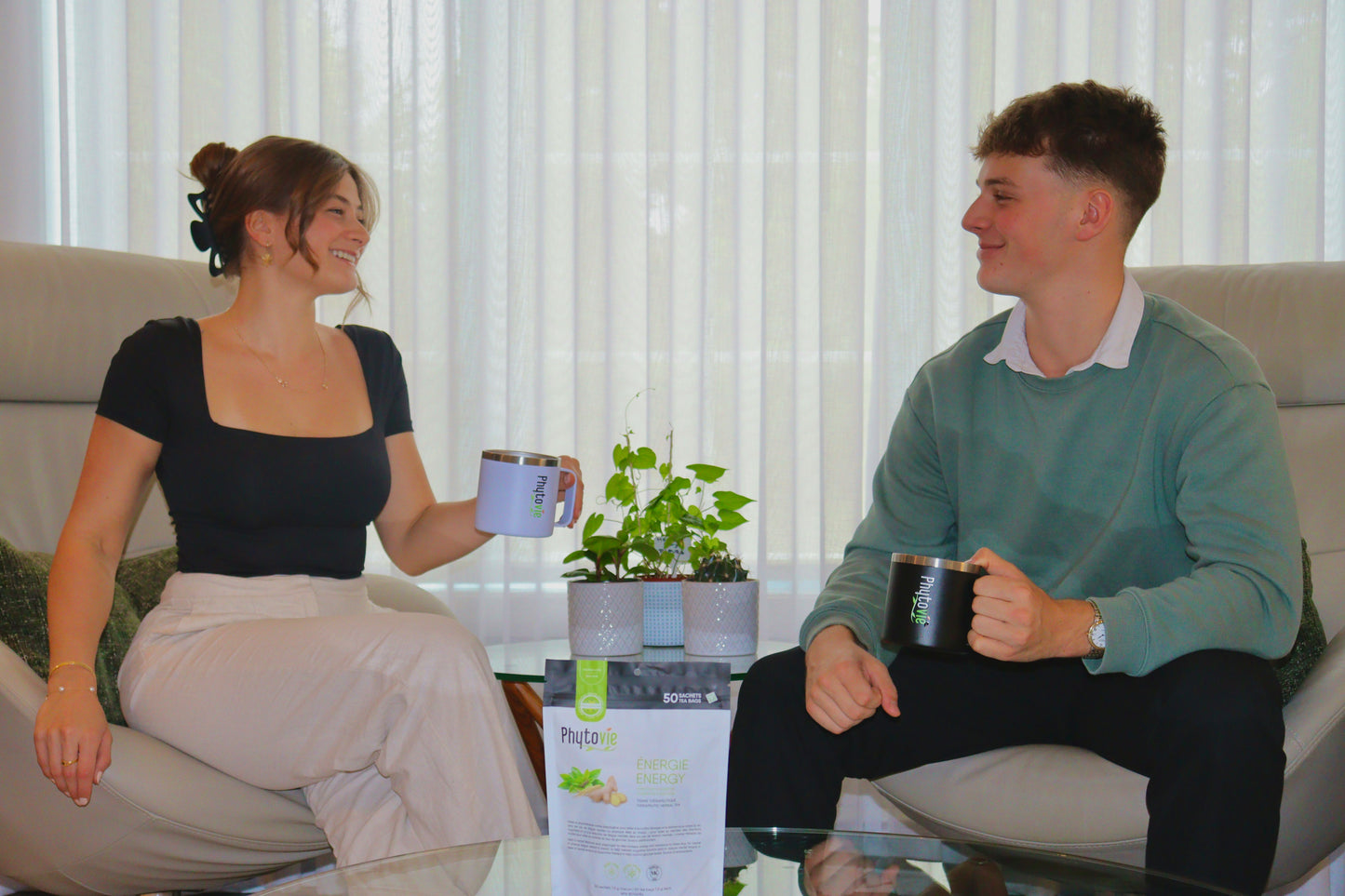 Image de deux personnes tenant des tasses d’infusion avec le sac de Tisane Énergie Phytovie au premier plan, illustrant un moment de bien-être et de partage.