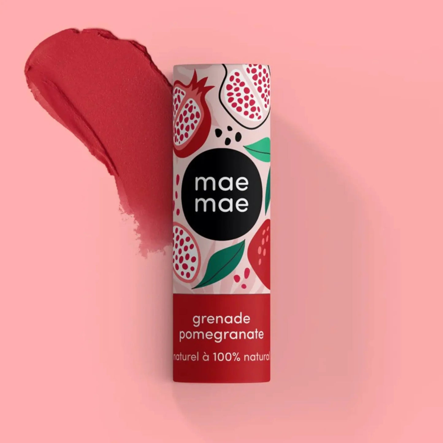 Mae Mae pomegranate lip balm displayed upright on a soft pink background, with a wide red lipstick smear behind the tube highlighting the balm’s tint.