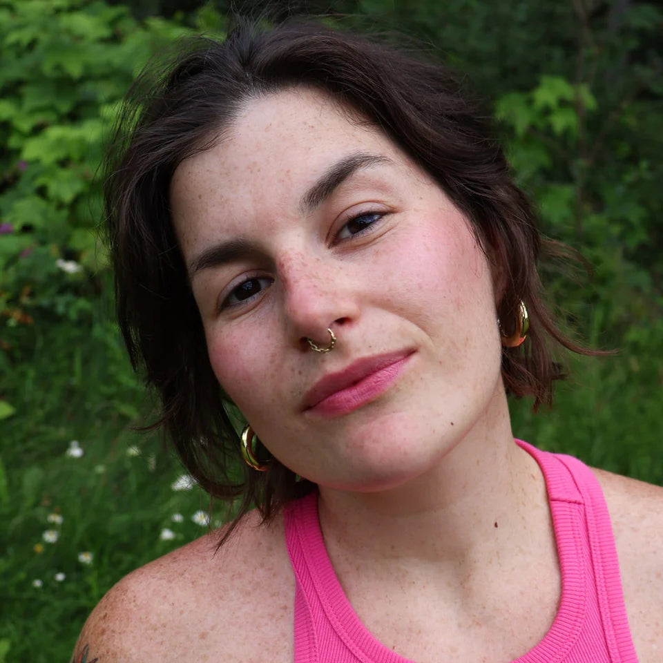 Portrait en extérieur montrant des lèvres naturellement teintées en rose avec le baume à lèvres au fruit du dragon, entourées de végétation verte.

